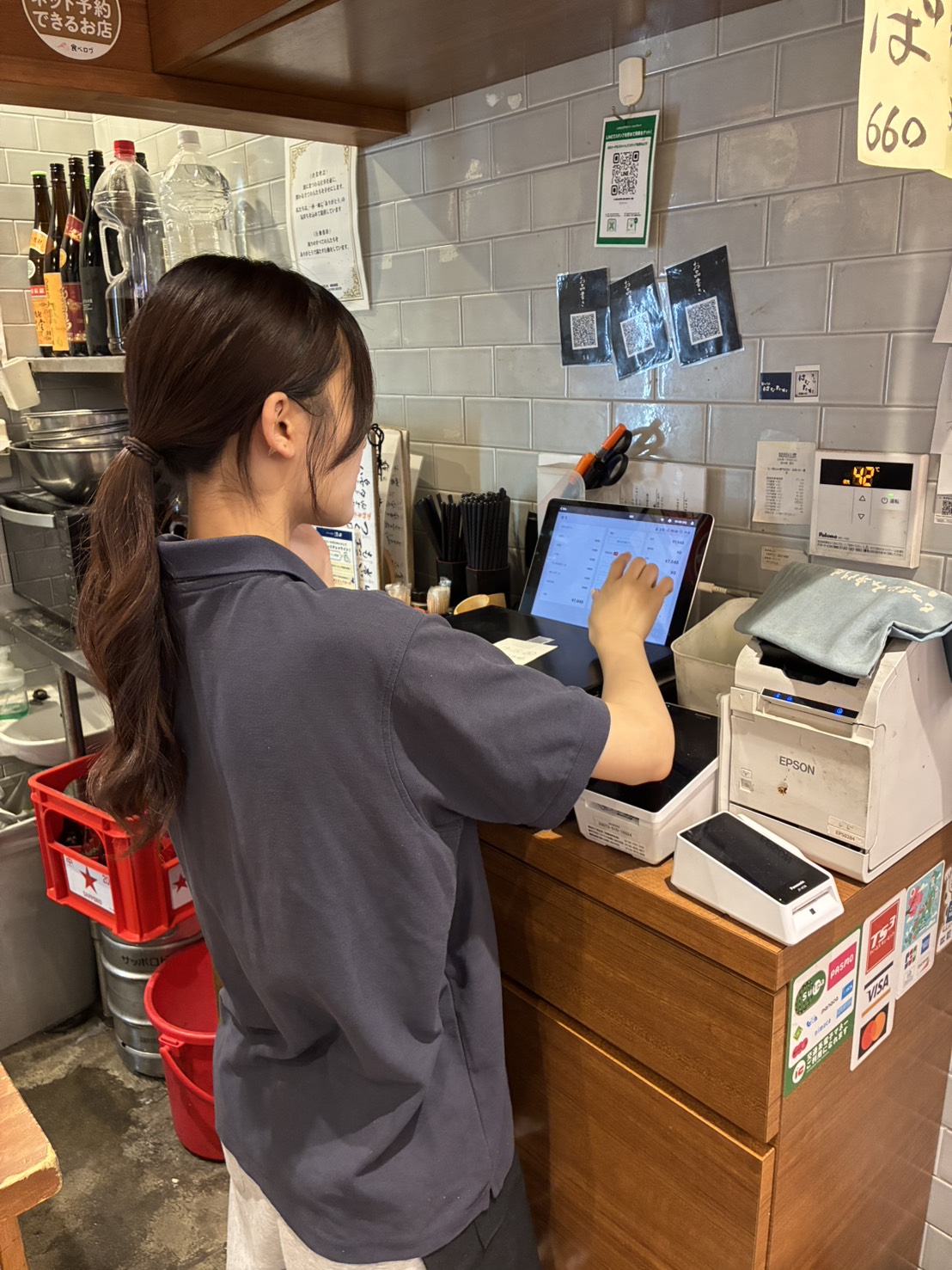 台上にはダイニーの管理画面と会計画面を開いたiPadが置かれ、スタッフはレジ前に立って画面を操作