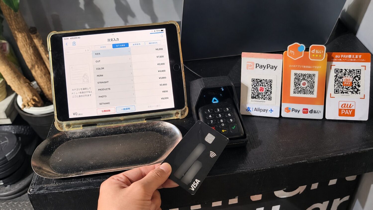 Airレジを表示したタブレットとAirペイのカードリーダー、手に持ったクレジットカード