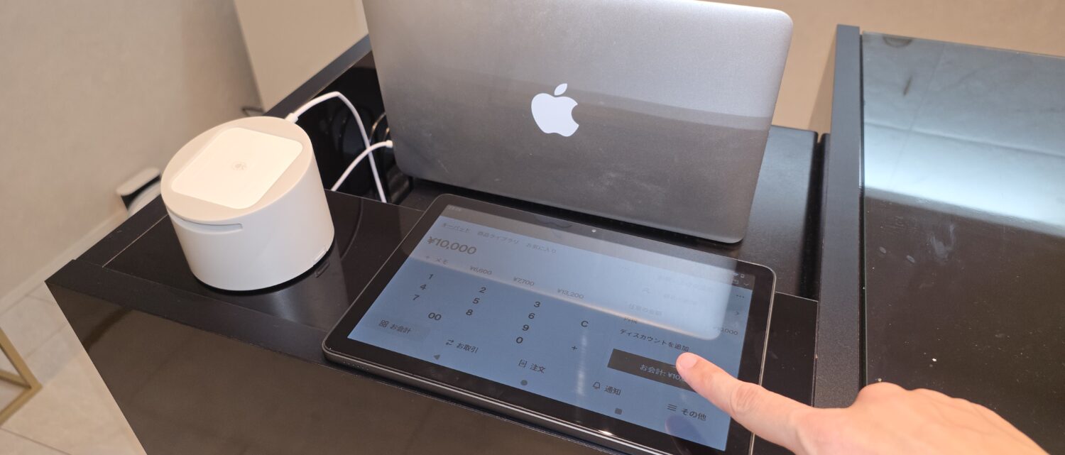 Square POSレジの金額入力画面を表示したタブレットを操作する手と、隣にあるSquareリーダー