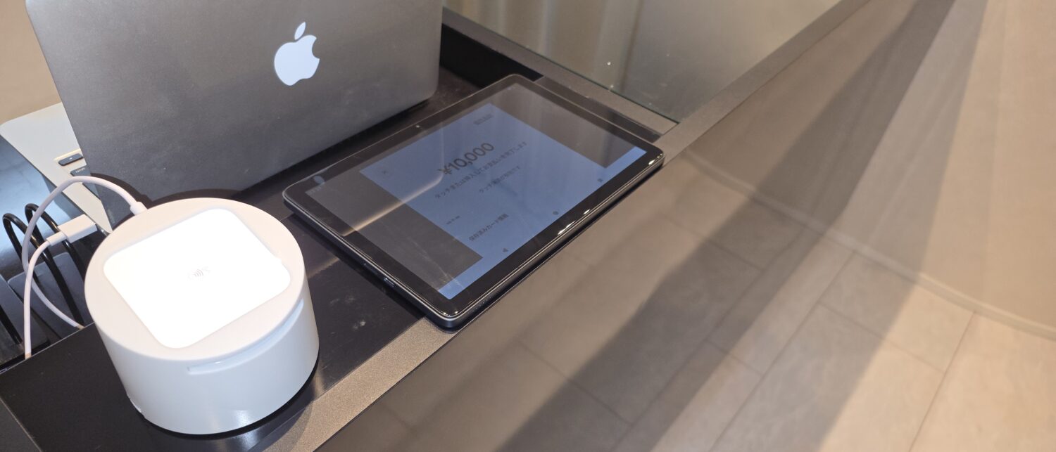 カードのタッチや挿入を案内するSquare POSレジの画面と、カウンターに置かれたSquareリーダー