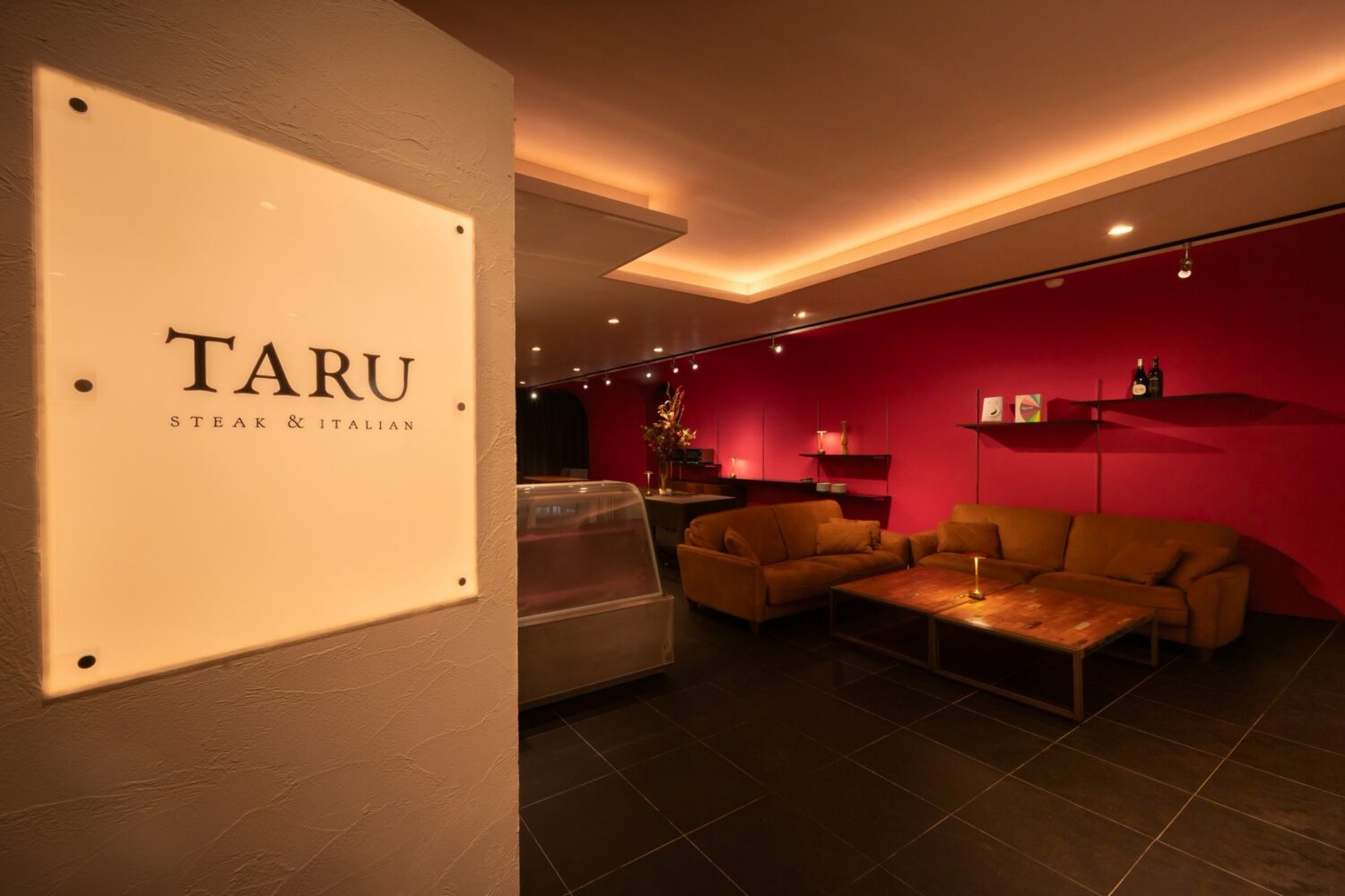 ARU steak&italianの店名看板と赤い壁にソファを配した店内